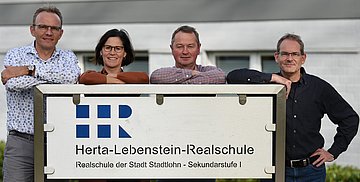 Leitung der Verwaltung vor dem Schullogo 