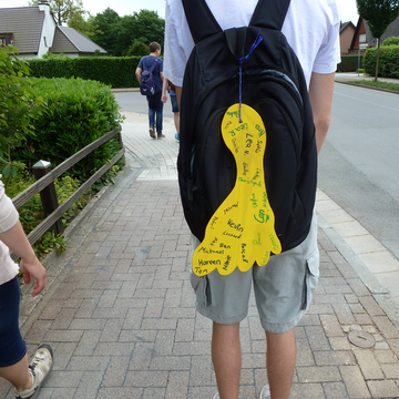 Schüler mit gebastelten Fuß und Unterschriften der Schüler aus Pappe am Rucksack auf dem Bürgersteig 